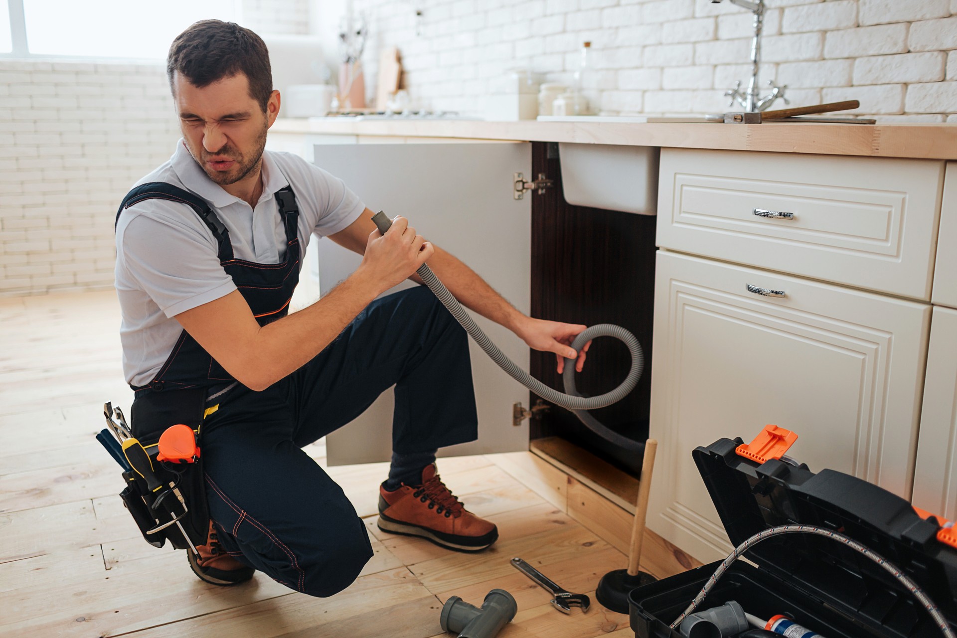 Young man hold hose in hand. Bad smell. Stinks. Handyman suffer from it. Opened toolbox and piece of pipe on floor.